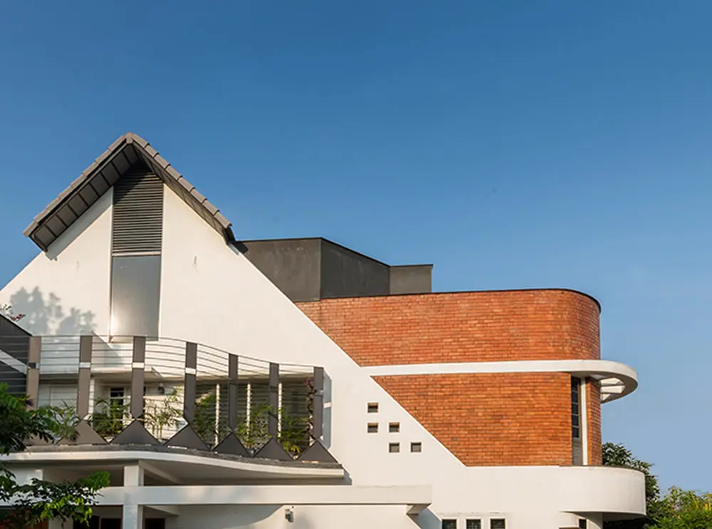Exterior of house with pitched roof, exposed brick curved wall, circular balcony edge and blue sky