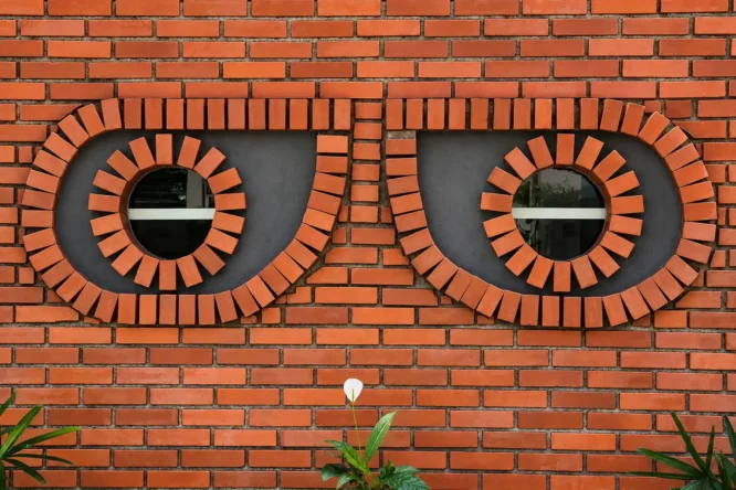 Brick facade with two large eye-shaped brick motifs and round openings above plants, Drishti Eye Clinic